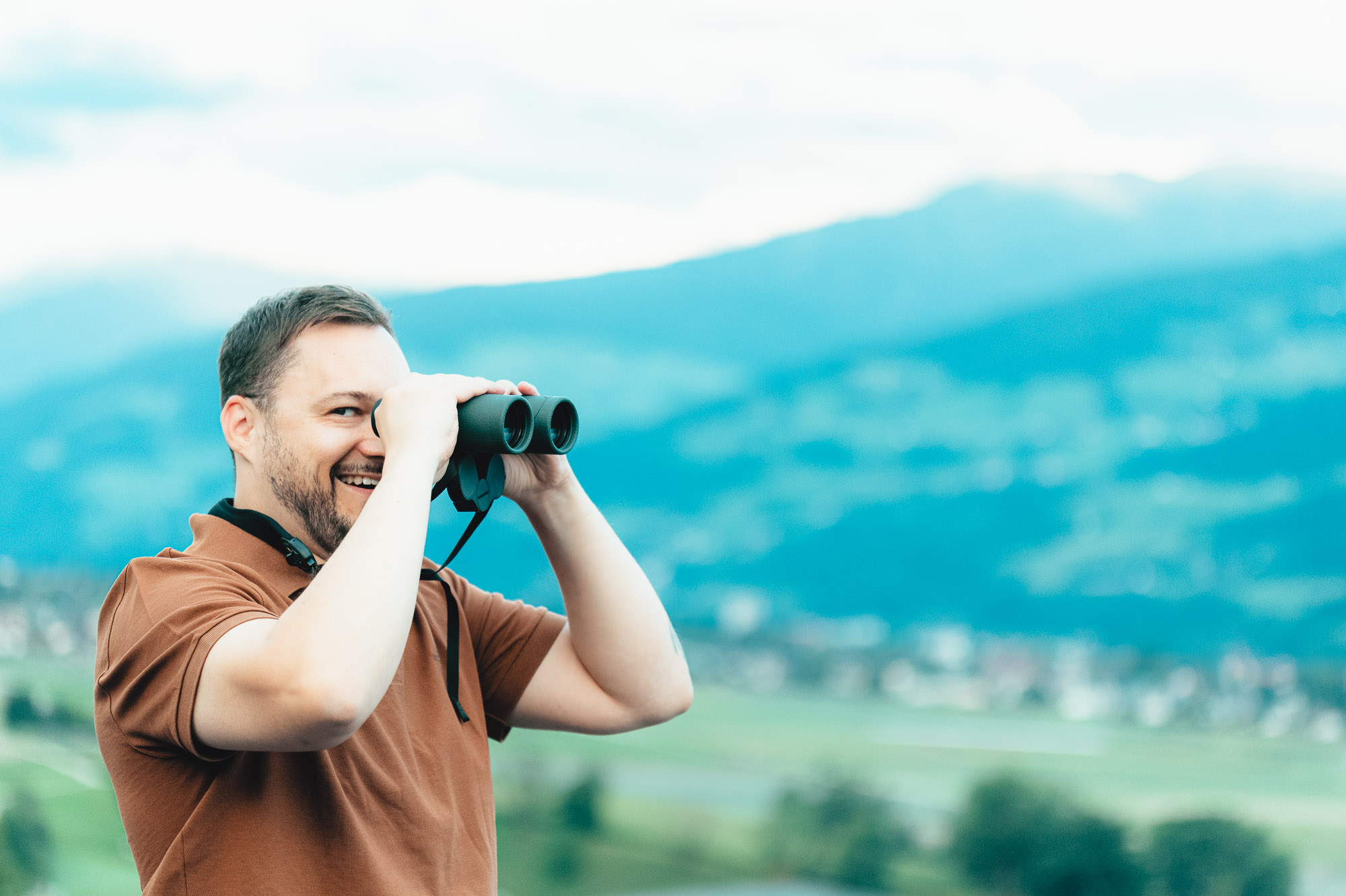 Immobilienberater Fabian blickt mit Fernglas auf der Suche nach Immobilien über die Landschaft