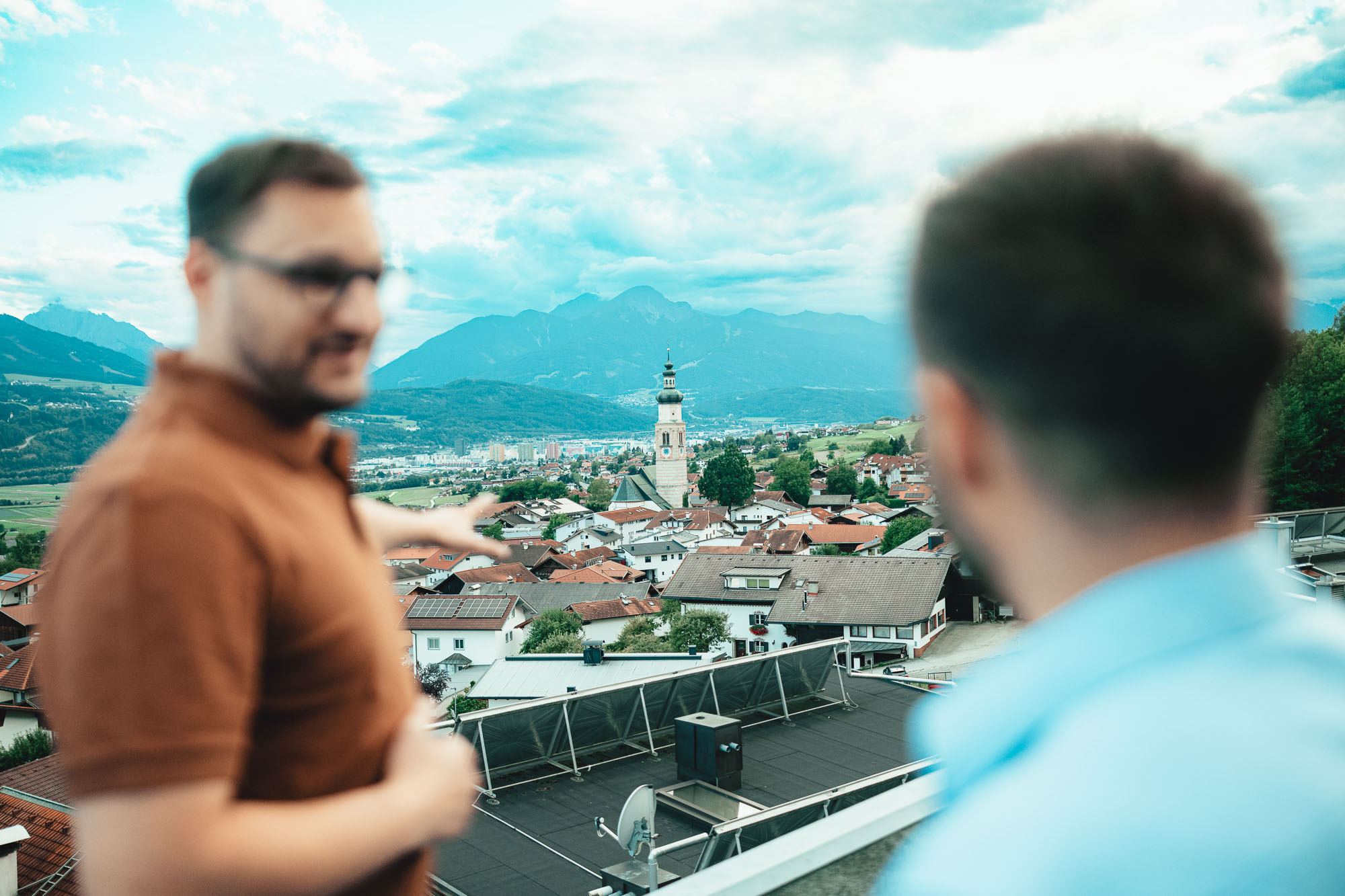 Fabian zeigt einem Kunden auf einer Dachterrasse die Aussicht auf eine Tiroler Stadt